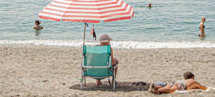 Mand sidder på stranden under parasol