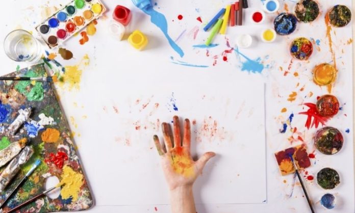 hand on white canvas surrounded by paints and brushes