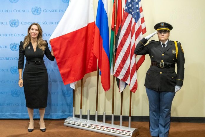 Vanessa Frazier (left), Permanent Representative of Malta to the United Nations, stands next to the flag of her country at the Installation Ceremony of Non-Permanent Members of Security Council for 2023-2024.