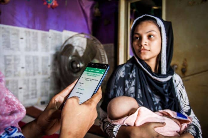 A woman holding a baby in the background and a person holding a phone in the foreground