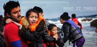 Un enfant dans les bras d'un homme au bord de la mer. Ce sont des refugies qui viennent d'acoster