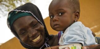 Femme nigérienne tenant dans les bras son enfant. Il porte un bracelet montrant qu'il est sorti de la malnutrition