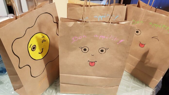 Sac en kraft contenant des paniers repas, illustré avec des yeux et des sourires