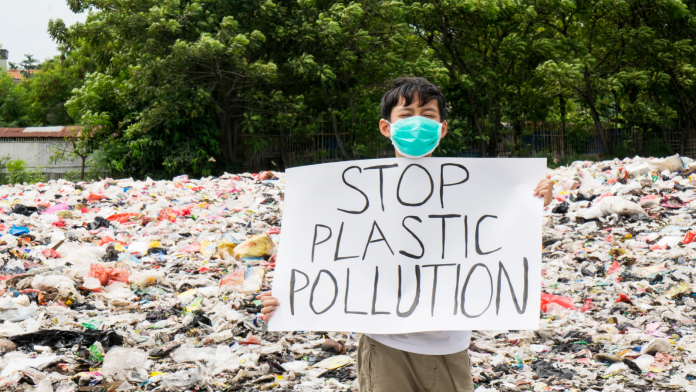 Enfant tenant une pancarte stop à la pollution plastique sur une plage pleine de plastique