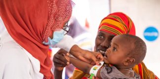 Une médecin mesure la circonférence du bras d'un bébé dans les bras de sa mère.