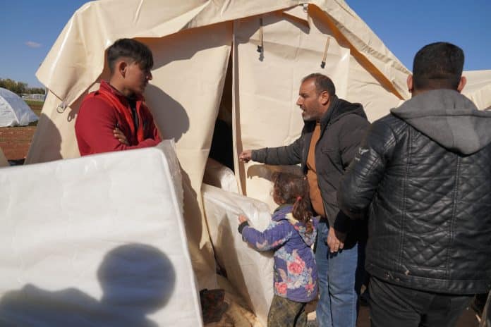 Des victimes rescapées du séisme devant une tente blanche recevant de l'aide humanitaire, en l'occurence des matelas.