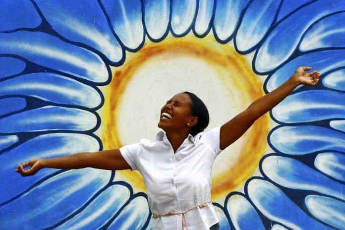 image d'une jeune fille souriante posant bras ouvert devant une image de fleur jaune sur fond bleu