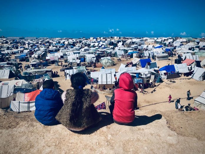 Trois enfants sur une colline face à une camp de déplacés