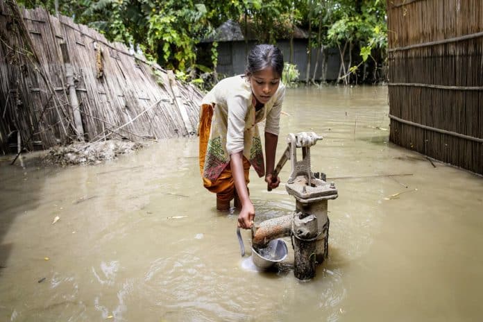 Ung stúlka reynir að pumpa vatni á flóðasvæði í Bangladesh 2016