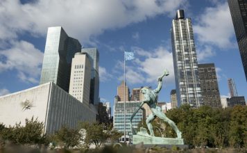 A view of the bronze sculpture "Let Us Beat Our Swords into Ploughshares" by Evgeny Vuchetich, presented to the United Nations in 1959 by the Government of the Soviet Union. In the background is part of the General Assembly building with a sculpture by Ezio Martinelli. UN Photo/Rick Bajornas